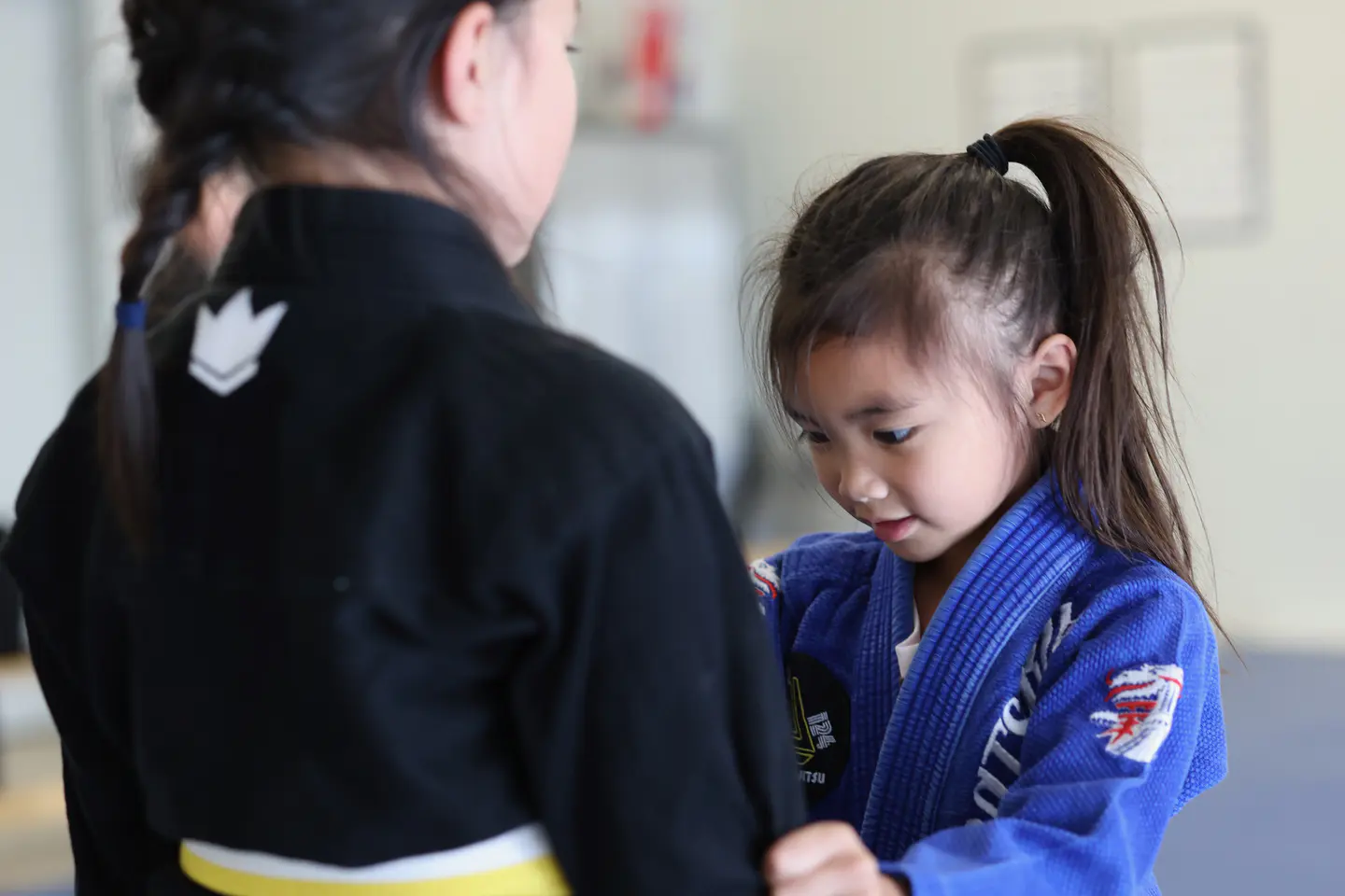 An older student helps a younger Munchkins student practise gripping during class
