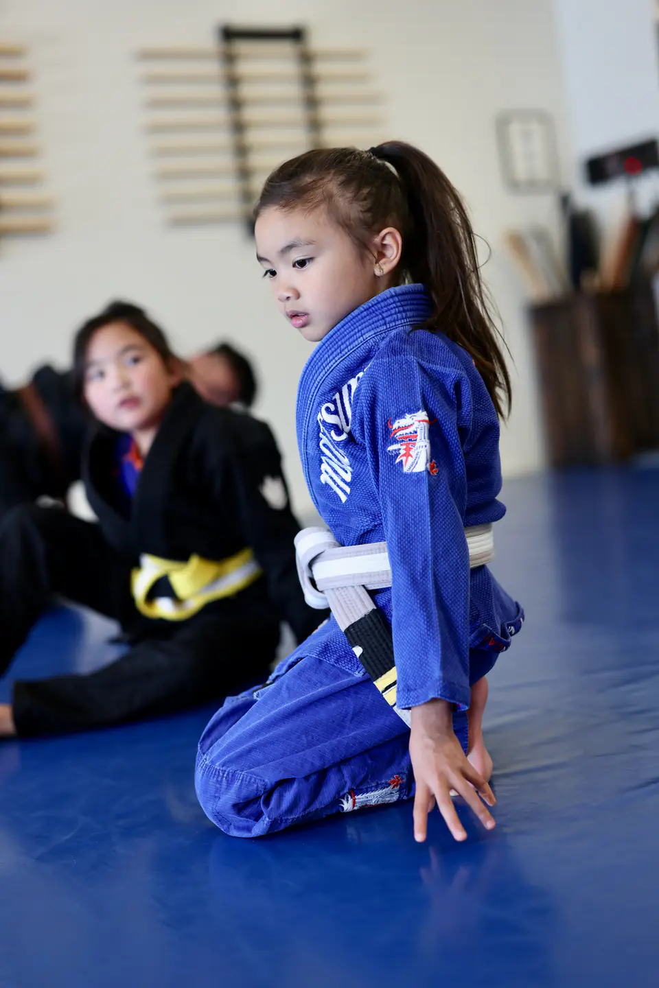 A young Munchkins student kneels on the blue mats between activities